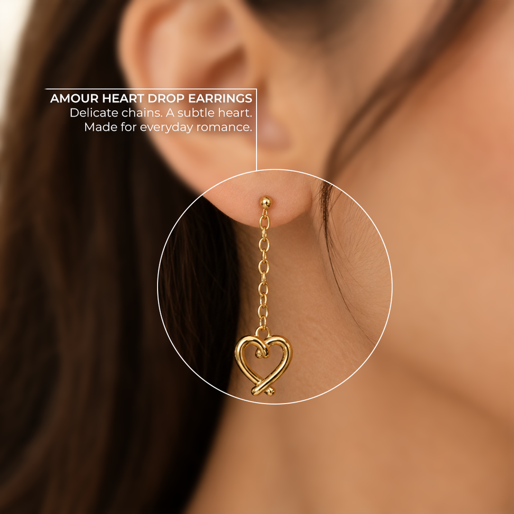 Amour Heart Drop Earrings by Ranaai, featuring a polished gold-tone heart charm and delicate chain detail worn on the ear against a softly blurred background.