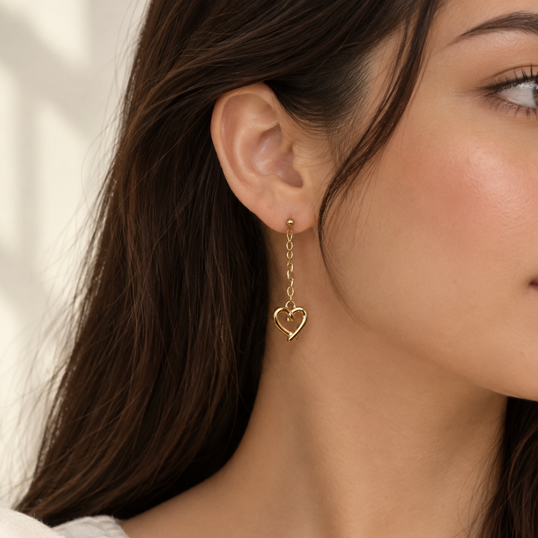 Amour Heart Drop Earrings by Ranaai worn on the ear, featuring a delicate gold-tone chain and polished heart-shaped charm.