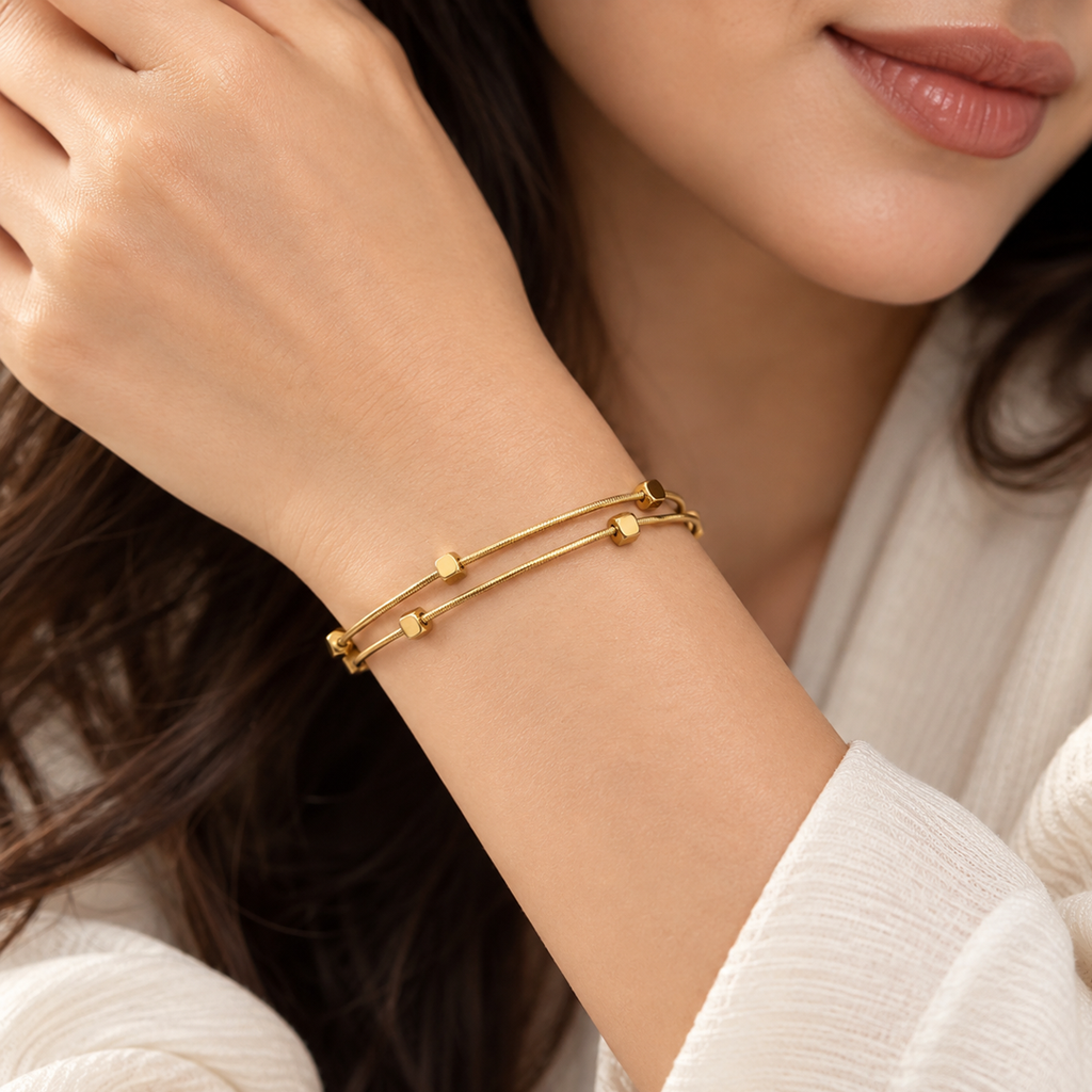 Lumière Double Layer Bracelet worn on a woman’s wrist, featuring two delicate gold-tone strands with geometric details.