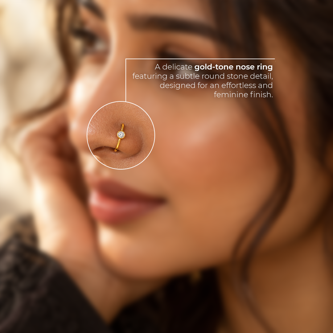 Close-up of a delicate gold-tone nose ring with a round clear stone, highlighting its polished finish and fine detailing.