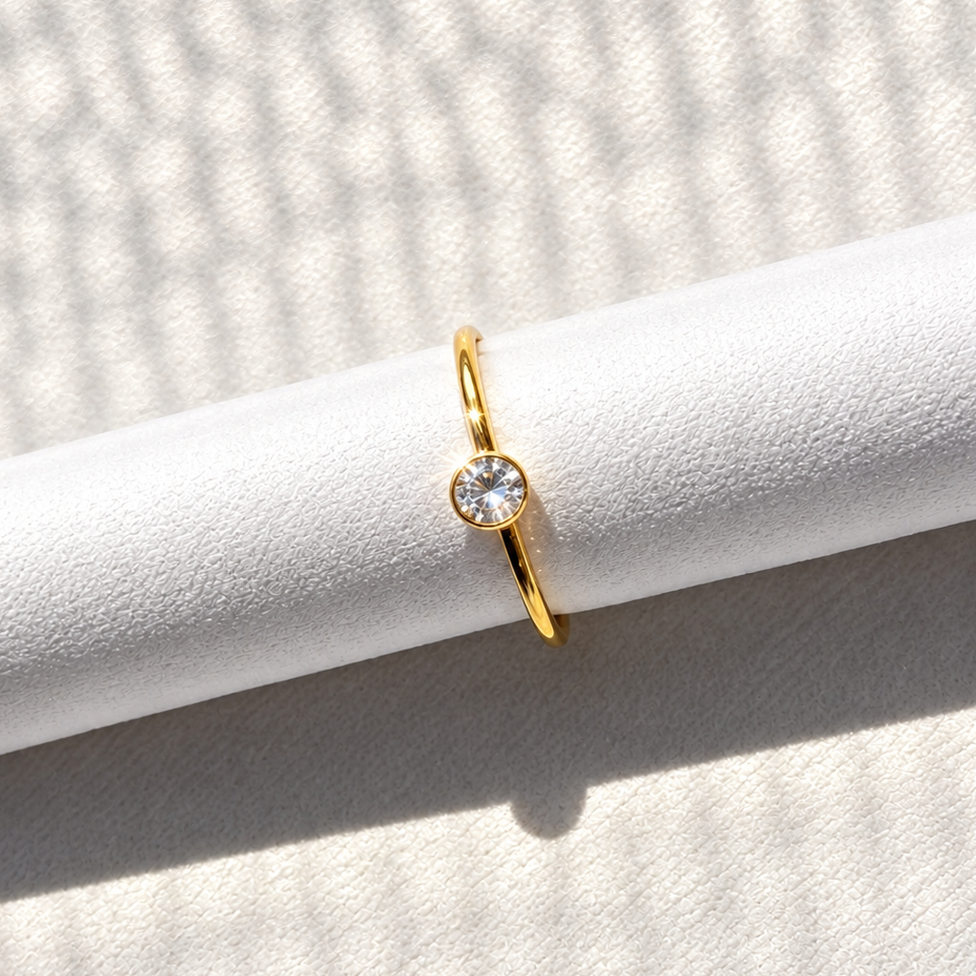 Gold-tone nose ring featuring a round clear stone detail, displayed on a white textured surface in natural light.