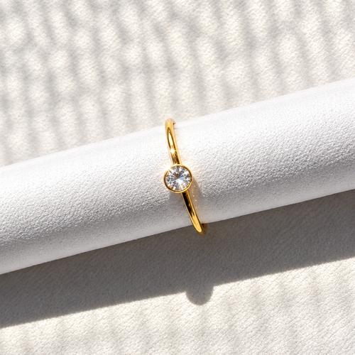 Gold-tone nose ring featuring a round clear stone detail, displayed on a white textured surface in natural light.